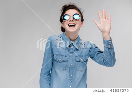 Young brunette girl in round glasses. Hairs are gathered in a bun. The girl says hello. Young brunette girl in round glasses. Hairs are gathered in a bun. The girl says hello. 41637079
