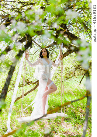 Seductive young bride in white negligee and lingerie standing on a white swing 41659181