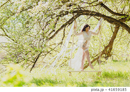 Seductive young bride in white negligee and lingerie standing on a white swing 41659185