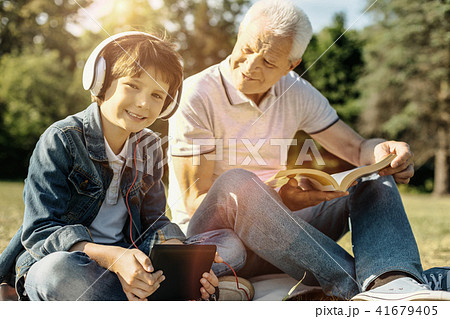 Smiling boy with his tablet and headphones sitting with grandpa Smiling boy with his tablet and headphones sitting with grandpa 41679405