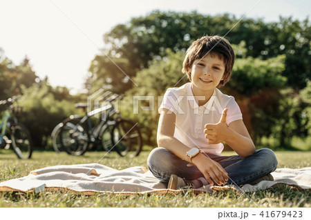 Smiling boy sitting on the grass and showing thumb up 41679423