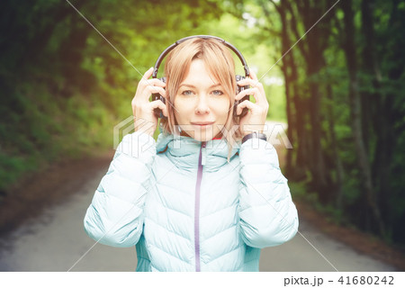 Portrait of a beautiful young woman holding headphones listening to music outdoors in the forest Portrait of a beautiful young woman holding headphones listening to music outdoors in the forest 41680242