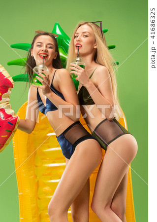 Cute girls in swimsuits posing at studio. Summer portrait caucasian teenagers on green background. 41686325