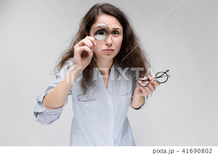 Young brunette girl with glasses. A girl looks through a magnifying glass. 41690802