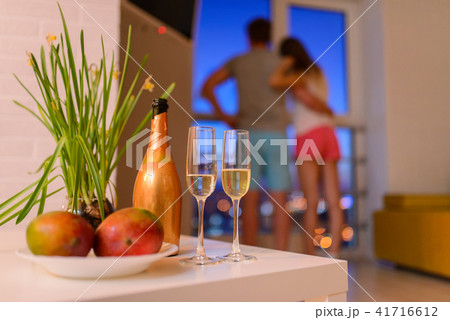 Bottle and two glasses of champagne on coffee table in living room, couple in love embraced at 41716612