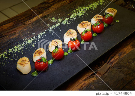 Fried scallops with tomatoes on a black plate. Shallow dof. Fried scallops with tomatoes on a black plate. Shallow dof. 41744904