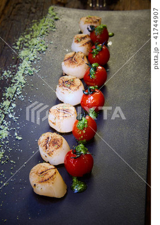 Fried scallops with tomatoes on a black plate. Shallow dof. Fried scallops with tomatoes on a black plate. Shallow dof. 41744907