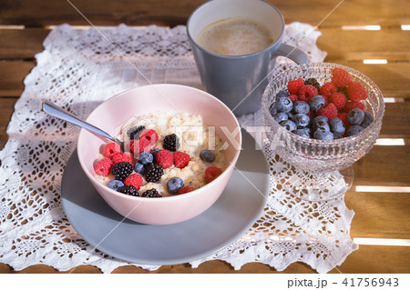 Healthy breakfast - oatmeal with fresh berries in a bowl with a cup of coffee Healthy breakfast - oatmeal with fresh berries in a bowl with a cup of coffee 41756943