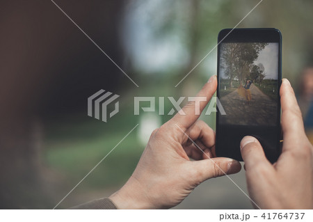Husband taking photo of wife posing on mobile phone Husband taking photo of wife posing on mobile phone 41764737