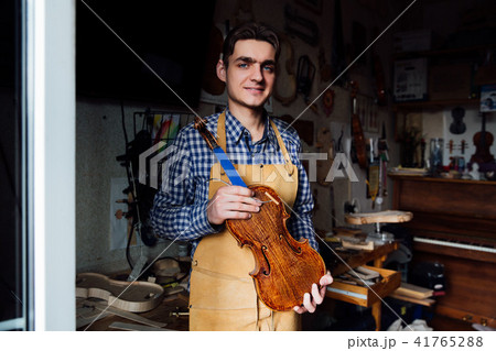portrait of a young luthier with a handcrafted violin in his workshop with the tools. portrait of a young luthier with a handcrafted violin in his workshop with the tools. 41765288