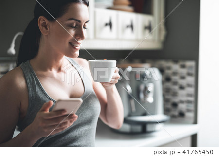 Relaxed woman drinking hot drink and using phone at home Relaxed woman drinking hot drink and using phone at home 41765450
