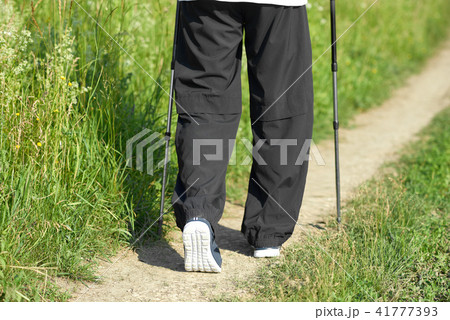 Man walking on green field's sandy path, using tracking sticks. Man walking on green field's sandy path, using tracking sticks. 41777393