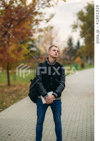 Stylish guy in black jucket stand in park. He hold a notebook in hands 41801926
