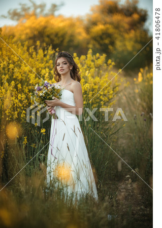 Beautiful young bride is wearing white dress holding fashion bouquet of wildflowers in yellow field Beautiful young bride is wearing white dress holding fashion bouquet of wildflowers in yellow field 41806478
