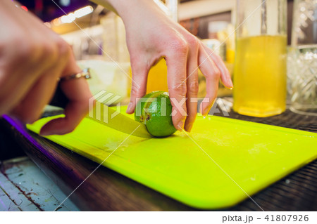 A close-up picture of bartender's hands cutting a raw, ripe and fresh green lime on a black cutting A close-up picture of bartender's hands cutting a raw, ripe and fresh green lime on a black cutting 41807926