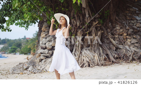 Young brunette pretty woman with long hair in white drees and hat posing on tropical beach 41826126