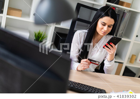 A young girl is sitting at the table, holding a bank card and phone. A young girl is sitting at the table, holding a bank card and phone. 41839302