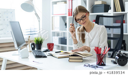 A young girl sits at a table in the office and holds a pencil in her hand. Before the girl lies an A young girl sits at a table in the office and holds a pencil in her hand. Before the girl lies an 41839534