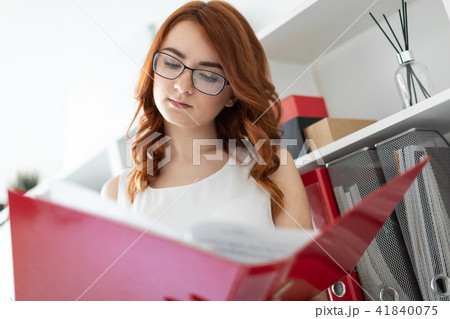A beautiful young girl stands near a stack in the office and holds a folder with documents in her 41840075