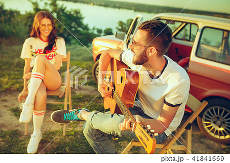 Couple sitting and resting on the beach playing guitar on a summer day near river Couple sitting and resting on the beach playing guitar on a summer day near river 41841669