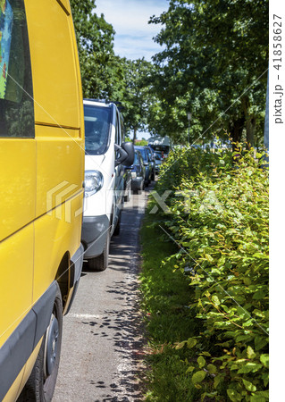 Row of cars parking on the street next to hedge 41858627