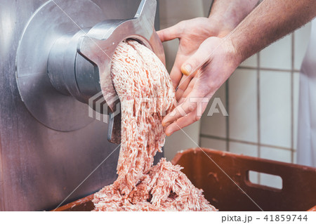 Minced meat flowing out of grinder in butchery 41859744