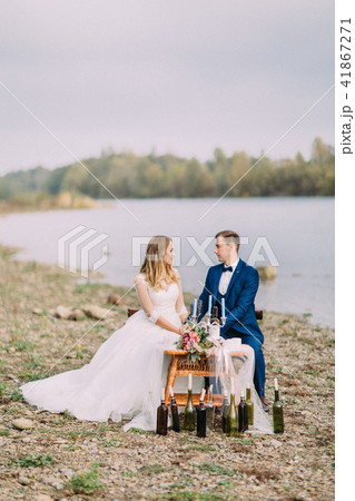 Happy newlyweds are holding hands while sitting at the wedding table on the coast. Vertical photo. 41867271