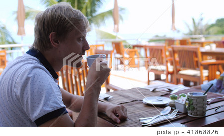 Young handsome sad man eating breakfast sitting in a beach cafe drink tea Young handsome sad man eating breakfast sitting in a beach cafe drink tea 41868826