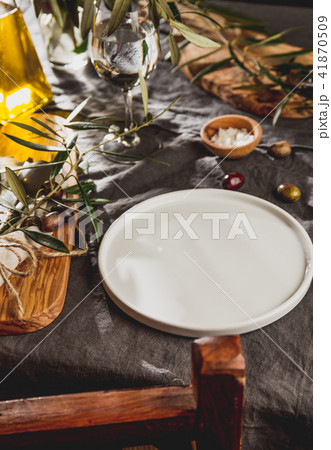 Table setting with gray Linen tablecloth and napkin, white plate, cutlery and and olive tree branch 41870509