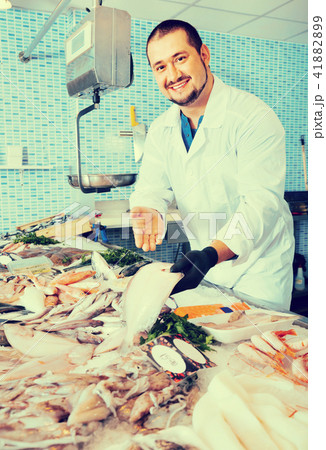 Man in glove behind counter shows fish in his hand Man in glove behind counter shows fish in his hand 41882899