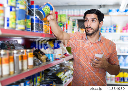 Man is choosing conserved peas using note list in supermarket. Man is choosing conserved peas using note list in supermarket. 41884080