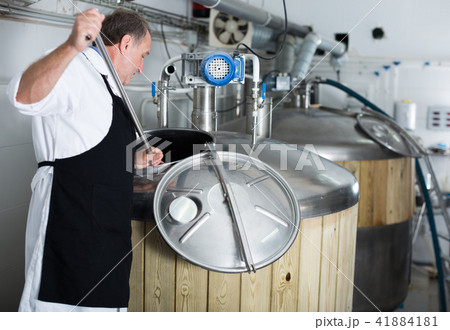 Adult brewer is standing with tube near reservoir for beer Adult brewer is standing with tube near reservoir for beer 41884181