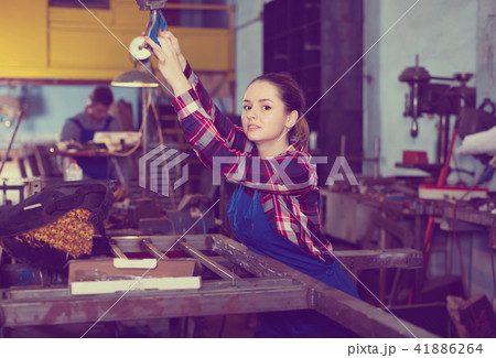 Girl worker is holding lift hook equipment in workshop. Girl worker is holding lift hook equipment in workshop. 41886264