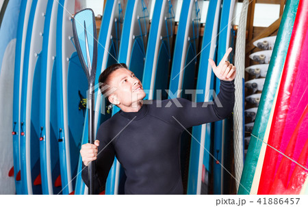 Portrait of sports young man in wetsuit holding paddle in surf club 41886457