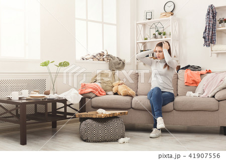 Desperate woman sitting on sofa in messy room 41907556