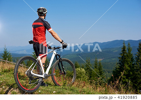 Back view of athletic cyclist stopped on top of hill to enjoy beautiful view of distant mountains 41920885