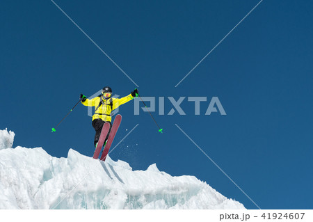 A jumping skier jumping from a glacier against a blue sky high in the mountains. Professional skiing 41924607