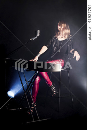 Blonde girl musician pianist plays perform on white digital piano, sits on chair, sings into retro Blonde girl musician pianist plays perform on white digital piano, sits on chair, sings into retro 41927704