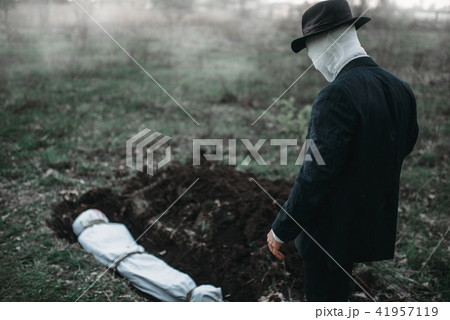 Bloody murderer stands against a grave with victim 41957119