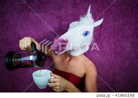 Funny girl unicorn pours tea. Freaky young woman in comical mask Funny girl unicorn pours tea. Freaky young woman in comical mask 41960398