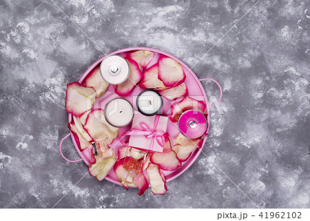 candles with rose petals on pink tray, cosmetics and gift box on gray stone background 41962102