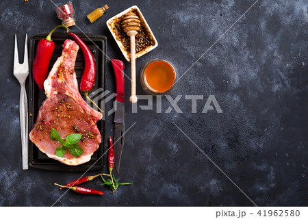 Raw steaks and frying pans with seasoning, garnishes and ingredients on a dark rustic background Raw steaks and frying pans with seasoning, garnishes and ingredients on a dark rustic background 41962580