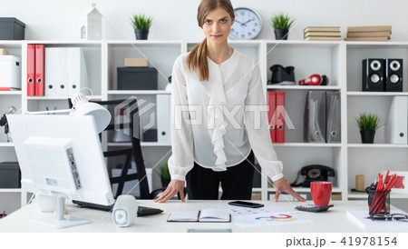 A young girl is standing right next to a table in the office. 41978154