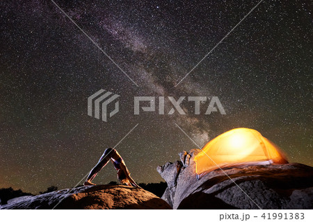 Attractive girl doing gymnastic exercises on big boulder on dark blue starry evening sky 41991383