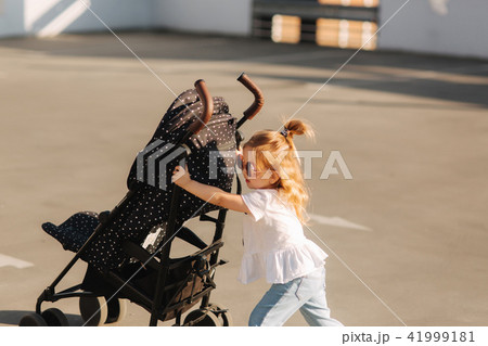 A little girl is pushing her baby carriage A little girl is pushing her baby carriage 41999181