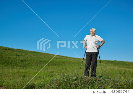Man wearing sportsuit standing with tracking sticks on green hill. Man wearing sportsuit standing with tracking sticks on green hill. 42009744
