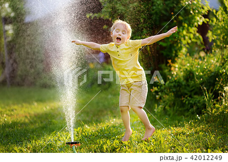 Funny little boy playing with garden sprinkler in sunny backyard Funny little boy playing with garden sprinkler in sunny backyard 42012249