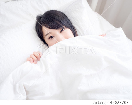 girl covers her face with white blanket in morning 42023703
