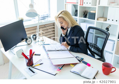 Young girl sitting at desk in office, talking on phone and looking at documents. Young girl sitting at desk in office, talking on phone and looking at documents. 42027901