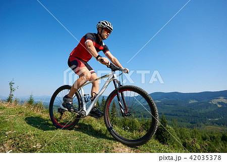 Young male sportsman cyclist in helmet, sunglasses and full equipment riding bike on grassy hill Young male sportsman cyclist in helmet, sunglasses and full equipment riding bike on grassy hill 42035378